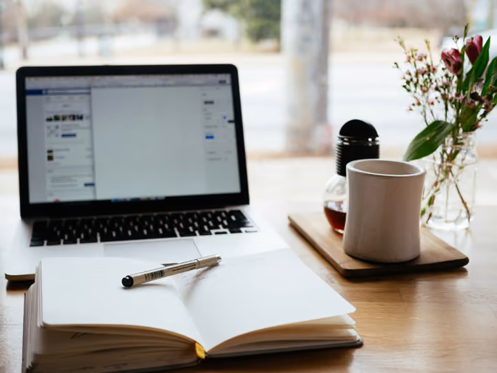 A laptop open on a discussion page, beside a notebook, a pen and a mug of coffee